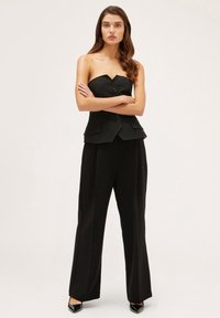 Top negro sin mangas con escote en forma de V y botones frontales, combinado con pantalones negros de talle alto y pierna ancha, junto con tacones negros.