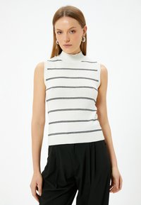 Biała bezrękawnik z golfem, w czarne poziome paski, z teksturowanej dzianiny, dopasowany fason, w zestawie z czarnymi spodniami o wysokim stanie.