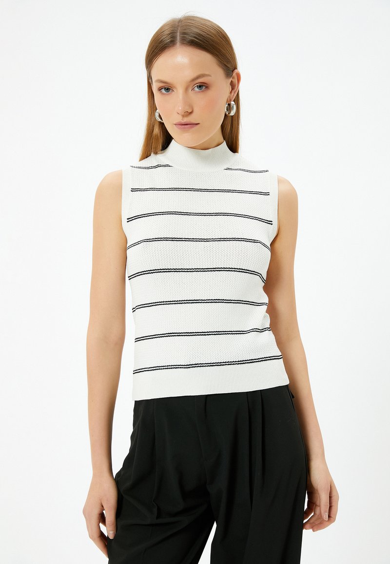 Biała bezrękawnik z golfem, w czarne poziome paski, z teksturowanej dzianiny, dopasowany fason, w zestawie z czarnymi spodniami o wysokim stanie.