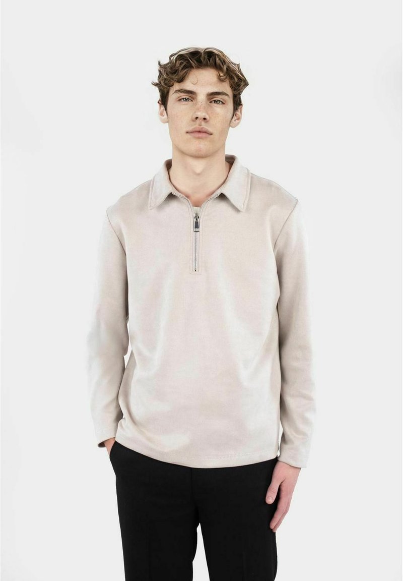 Ljust beige sweatshirt med zip-krage, långa ärmar och mjukt tyg. Har en ren design och rak skärning.