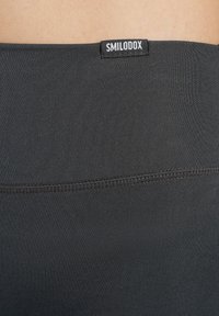 Leggings sportivi neri con una texture liscia, una forma aderente e un'etichetta con logo incorporata in vita. Le cuciture sono visibili.