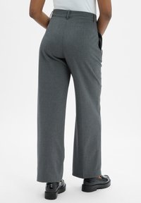 Pantalons larges gris en tissu texturé, avec des poches latérales et une taille cintrée, associés à des chaussures noires.