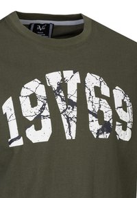 Olijfgroene T-shirt met ronde hals, voorzien van grote witte en zwarte gebarsten letters "1969" op de voorkant. Zachte katoenen stof.