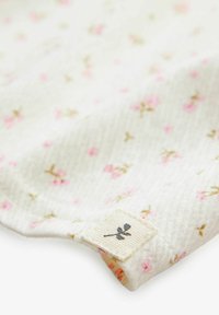 Leichte Stoff mit weißem Grund, der kleine rosa Blumenmuster und goldene Akzente aufweist. Enthält ein Stoffetikett mit einem Blätterdesign.