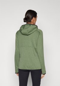 Sweatshirt de fecho éclair verde-claro com um acabamento texturizado, apresentando capuz, acabamentos pretos e um design ajustado. A vista traseira mostra detalhes de costura.
