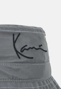 Chapéu de balde cinza feito de um tecido suave, com detalhes cosidos e um logotipo bordado em preto. A aba é larga e tem um ajuste descontraído.