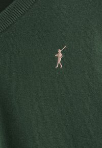 Pull en tricot vert avec une petite figurebrodée tenant un club de golf dans une couleur claire contrastante. Design en V avec un col en côtes.