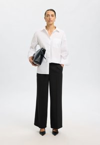 Bijela košulja s gumbima i džepom na prsima, crne hlače širokih nogavica, crna torbica s ručkom i crne cipele s šiljastim vrhom. Glatki materijal.