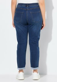 Granatowe dżinsy o luźnym kroju, z elastycznym pasem i podwiniętymi mankietami. Posiadają dwie tylne kieszenie oraz subtelne detale przeszyć.