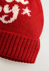 Bonnet en tricot rouge avec un revers côtelé, orné de texte blanc et de motifs d'étoiles sur la surface. Texture douce, design à couronne arrondie.