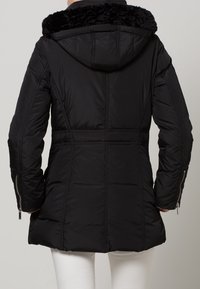 Giacca a vento nera con cappuccio texturizzato, vita cinchata e tasche laterali con zip. Presenta un design trapuntato e un morbido rivestimento.