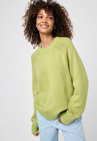 Helle grüne Strickpullover mit Rundhalsausschnitt und gerippten Bündchen. Kombiniert mit hellblauen Jeans, die eine lockere Passform und eine weiche Textur haben.