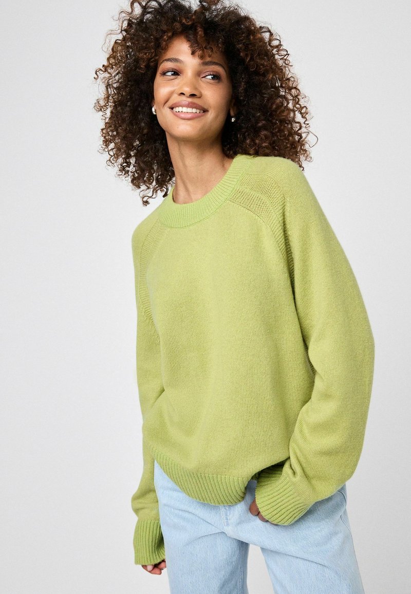 Helle grüne Strickpullover mit Rundhalsausschnitt und gerippten Bündchen. Kombiniert mit hellblauen Jeans, die eine lockere Passform und eine weiche Textur haben.