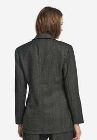 Blazer med svart-och-vitt fiskbensmönster, strukturerade axlar, skräddarsydd passform och en enda vent bak; slät textur och slagkrage.