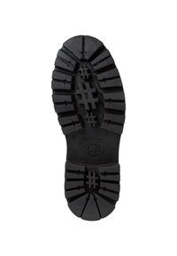 Suela de zapato de goma negra con surcos y treads profundos para agarre, con superficie texturizada y logo circular en el centro.
