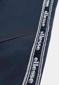 Tissu bleu marine avec une couture piquée et un ruban blanc et bleu marine marqué "ellesse" le long du bord.