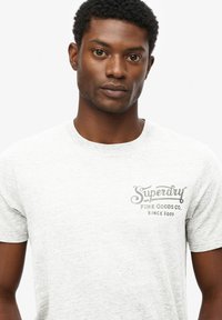 Camiseta gris de manga corta hecha de una tela suave. Presenta un logo impreso en el área del pecho izquierdo. Corte regular y diseño de cuello redondo.