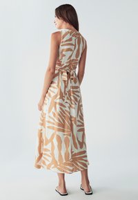 Maxi obleka z bež in belo abstraktno vzorcem, brezrokavni dizajn, detajl vezanja na hrbtu in tekoča tkanina. Lahka tekstura in sproščen kroj.