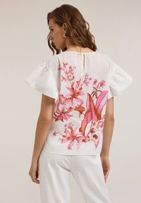 Blusa bianca con ricami floreali in tonalità di rosa e arancione. Presenta maniche arricciate e una chiusura a bottoni sul retro.