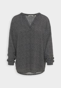 Blusa bianco e nero con scollo a V, maniche lunghe e vestibilità comoda. Presenta un motivo a pois sparsi su un tessuto leggero e testurizzato.