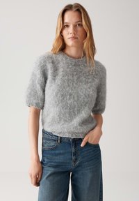 Jasnoszary, krótkorękawowy sweter z dzianiny o miękkiej, puszystej teksturze, zestawiony z wysokim stanem niebieskimi dżinsami. Prosty okrągły dekolt i luźny krój.