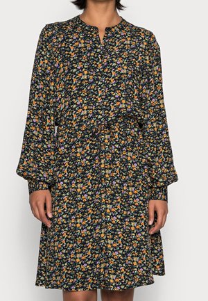 Femme portant une robe noire à manches longues, longueur genou, avec un petit imprimé floral multicolore et des boutons sur le devant.