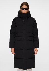 Svart puffjacka med huva, tryckknappsstängning, två framfickor och en quiltad design, med en matt finish och knälång längd.