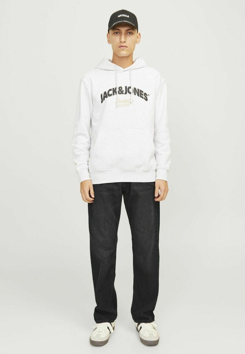 Szara hoodie z czarnym tekstem logo, z przednią kieszenią. W połączeniu z ciemnymi dżinsami i białymi sneakersami, na głowie czapka w kolorze czarnym.