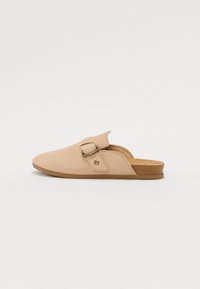 Scarpe beige in suede slip-on con punta arrotondata, cinturino regolabile e soletta in sughero, caratterizzate da un design minimalista e una texture morbida.