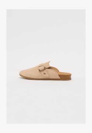 Beige suede slip-on shoe with a rounded toe, adjustable strap, and cork insole, featuring a minimal design and soft texture.