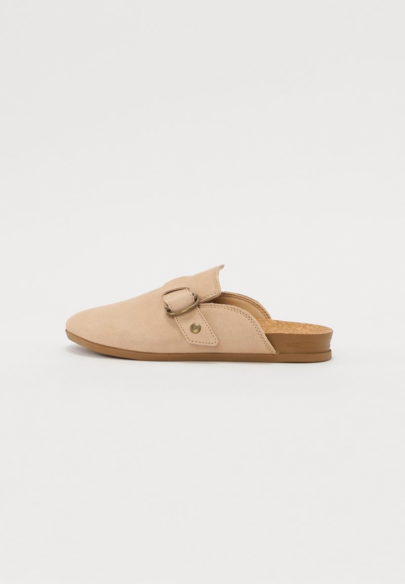 Scarpe beige in suede slip-on con punta arrotondata, cinturino regolabile e soletta in sughero, caratterizzate da un design minimalista e una texture morbida.