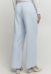 Lichtblauwe wijde broek met een elastische tailleband, gemaakt van een gestructureerde stof. Zijzakken en een relaxte pasvorm, gecombineerd met witte hakken.