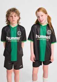 Svarta sporttröjor med en gr ön vertikal rand, korta ärmar och "hummel"-logotyp. Kombinera med svarta shorts och vita strumpor. Slät textur.