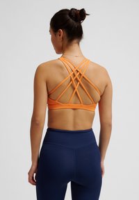 Oranje sportbeha met meerdere bandjes op de rug, met een gladde textuur. Gecombineerd met hooggeremde marineblauwe legging.