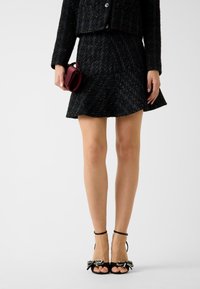 Blazer in tweed nero e gonna a ruota con riflessi blu. Décolleté nere con fiocchi decorati in argento. Piccola borsa bordeaux tenuta a mano.