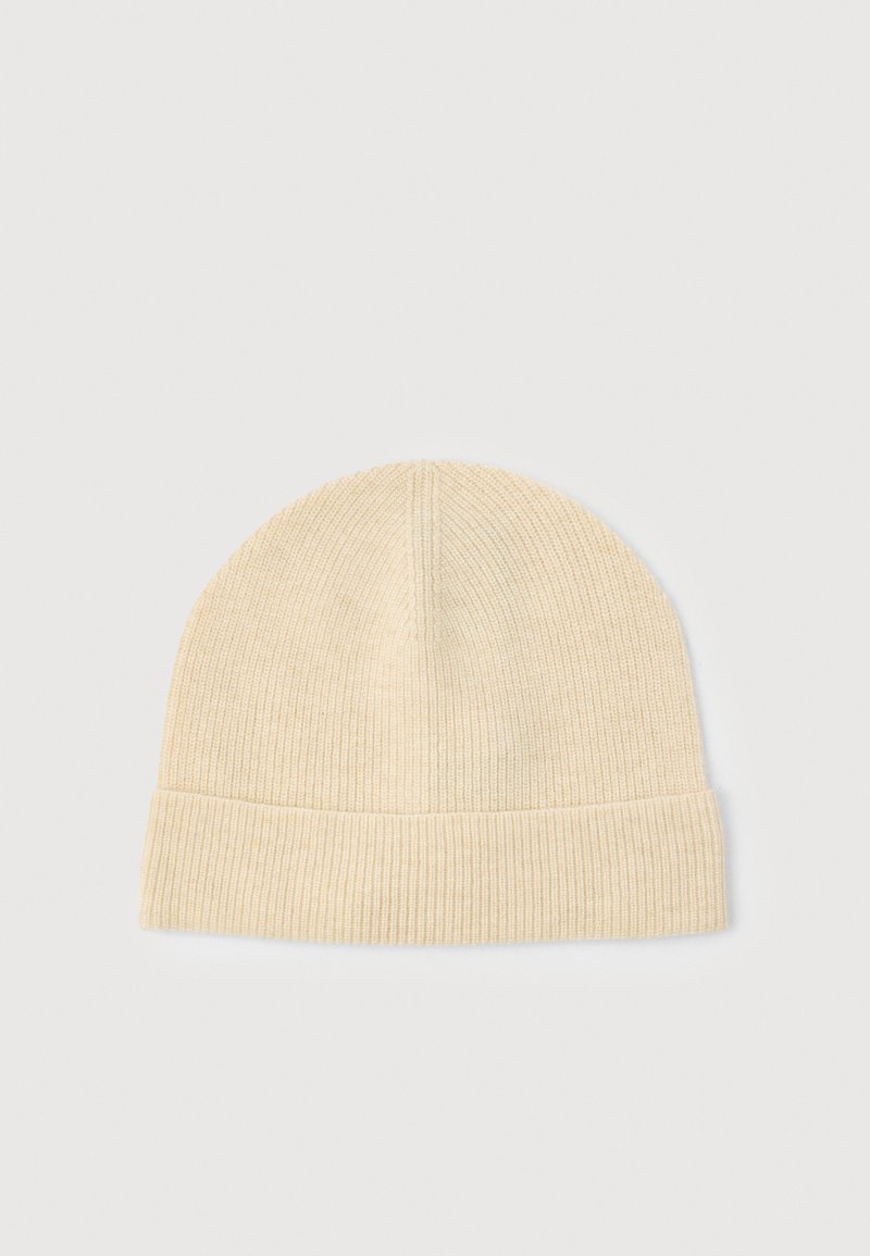 Gorro de punto en beige claro, con textura acanalada, parte superior redondeada y puño doblado. Material suave para confort y calidez.