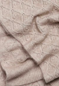 Helles rosa gestrickter Stoff mit einem Rautenmuster, der eine weiche, flauschige Textur aufweist. Die Kanten sind gerippt, was eine subtile Dimension hinzufügt.