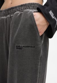 Pogled na roko v žepu temno sivih trenirk Karl Lagerfeld z elastičnim pasom in vezenim logotipom.