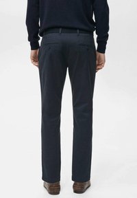 Dunkelblaue Hosen mit geradem Bein, zwei Gesäßtaschen und einem subtil strukturierten Stoff. Getragen mit braunen Schuhen.