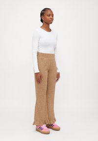 Lightweight white long-sleeve top paired with textured, beige flared pants featuring a ruffle hem and pink sneakers with brown accents.