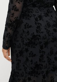 Juodas suknelė su gėlių raštu, pagaminta iš permatomo, švelnaus audinio. Ilgomis rankovėmis ir prigludusia siluetu su šone iškirpimu.