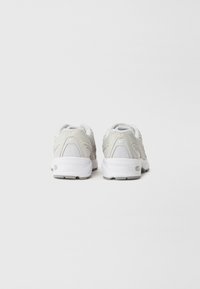 Light gray athletic shoes with a textured mesh upper, white sole, and reinforced heel. Features curved accents and a cushioned design for support.