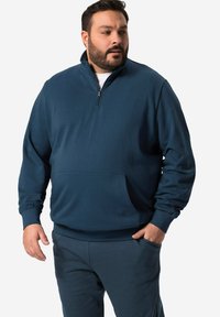 Tmavě modrá mikina na zip s vysokým límcem a přední kapsou. Má dlouhé rukávy a volný střih, vyrobena z měkké, texturované látky.