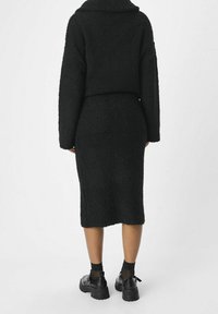 Ensemble tricoté noir et texturé comprenant un pull ample et une jupe ajustée, tous deux en tissu doux et duveteux. Associé à des chaussures noires imposantes.