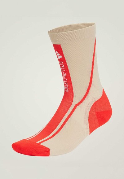 Calcetín deportivo en color beige y rojo con un puño acanalado, que presenta atrevidos acentos rojos en el cuerpo y en la puntera, diseñado para la comodidad y el rendimiento.