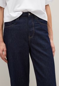 Jeans de mezclilla azul oscuro con un corte relajado, que cuentan con costuras amarillas, bolsillos frontales y un cierre de botón en la cintura.
