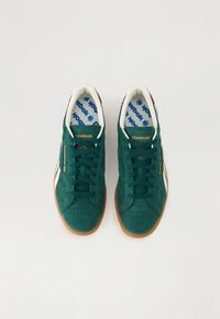 Zelené semišové tenisky s bílými akcenty, kulatou špičkou a černou patou. Mají ploché tkaničky a texturovanou gumovou podrážku.