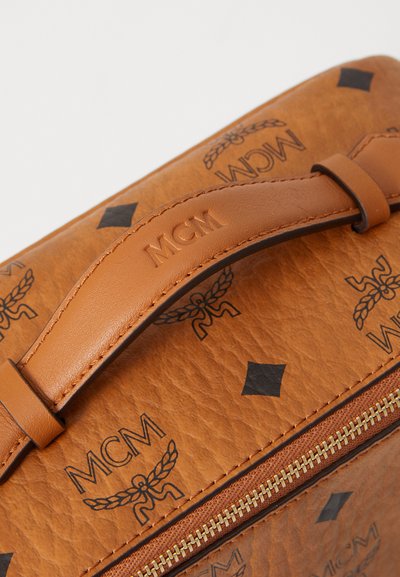 Braune Lederhandtasche mit prägierter MCM-Logo und schwarzen geometrischen Mustern, ausgestattet mit einem glatten Griff und goldenen Reißverschlussdetails.