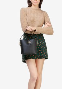 Borsa a secchiello nera in pelle con una forma strutturata, accessori in oro e manico superiore, esposta accanto a una gonna verde con un motivo marrone.