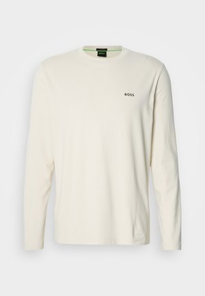 Camiseta de manga larga color crema hecha de algodón, con cuello redondo y un pequeño logo negro de "BOSS" en el pecho. Tela suave y ligera.